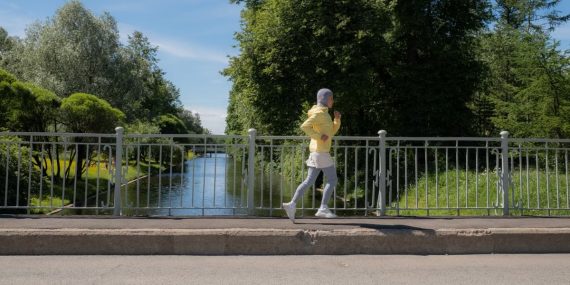 Muslim woman in hijab jogging along a picturesque park canal on a sunny day.